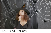 Beautiful girl witch in a witch's cap thought of something interesting against the background of a white web on Halloween. Стоковое видео, видеограф Катерина Белякина / Фотобанк Лори