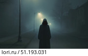 Mysterious figure in hooded cloak stands in foggy street illuminated by dim streetlights. Стоковое AI-видео, аниматор Данил Руденко / Фотобанк Лори