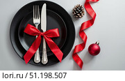 Christmas. Festive table. Black plate with silver cutlery tied with a red bow, surrounded by Christmas paraphernalia. AI generative. Стоковое AI-изображение, AI-художник Роман Дзюбало / Фотобанк Лори