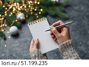 Woman's hand writing in empty notebook at the desk with Christmas decoration. Back to life, goal list. Plan, goals, checklist, idea concept. Top view, copy space. New Year. Blank White Paper Sheet. Стоковое AI-изображение, AI-художник Марина Демидюк / Фотобанк Лори