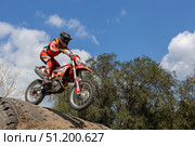 Magnitogorsk, Russian Federation - August 23, 2025: Male motocross rider in red gear jumps over dirt mound during enduro competition, showcasing skill and adrenaline in outdoor setting. Редакционное фото, фотограф Ирина Ручушкина / Фотобанк Лори