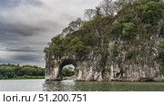A beautiful rock with an arched vault over the river. Steep slopes, green vegetation at the top. Clouds in the sky. China. Guilin. Elephant Trunk Hill. Taohua River. Стоковое фото, фотограф Вера Ивановна Кубарева / Фотобанк Лори