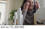 Attractive brunette senior woman putting on makeup looking in the mirror. Beautiful lady caring her face. Elderly female applied cosmetics. Natural old beauty and aging concept. Skin care and make-up. Стоковое видео, видеограф Марина Демидюк / Фотобанк Лори