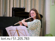 A woman in a floral dress plays the flute during a formal music performance, reading from sheet music in a concert hall. Стоковое фото, фотограф Андрей Журавлев / Фотобанк Лори