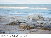 A rocky beach with a large rock in the foreground. The rock is partially submerged in the sand. The ocean is calm and the sky is cloudy. Стоковое фото, фотограф Наталия Кирсанова / Фотобанк Лори