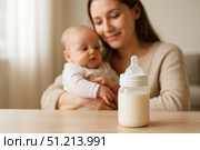 A tender moment between a mother and her baby as they bond over milk from a bottle, capturing the essence of nurturing and care in a cozy home environment. Стоковое AI-изображение, AI-художник Башкирова Анна / Фотобанк Лори