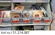 A store rack with spiral notebooks of A6 and A5 formats. In the foreground are bright covers with illustrations: cartoon characters in fantasy style, a portrait of a girl with big eyes and angelic elements, as well as images of cute animals - a hamster with wings and a wreath of flowers. Products of the Erich Krause brand are arranged in cells, each notebook is provided with a price tag with a promotional offer. Other notebooks and notepads in the assortment are visible below and on the side. The atmosphere of the photo conveys the variety of stationery products in the supermarket, aimed at schoolchildren, students and lovers of creative notepads. Редакционное фото, фотограф Анна Кривицкая / Фотобанк Лори