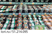 A store shelf with a large assortment of ready-made meals in packages under the Lenta Fresh brand. The products are presented in black plastic containers with a transparent lid and green labels. Various dishes are visible: pasta, meat cutlets, chicken with a side dish, noodles, vegetable stews, casseroles and other options. The packages are neatly laid out in rows on several shelves. The shelves also have price tags with promotional offers and discounts. The atmosphere of the photo emphasizes the convenience and variety of ready-made food intended for fast food at home or at work. Редакционное фото, фотограф Анна Кривицкая / Фотобанк Лори