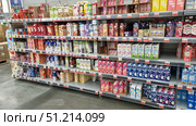 Supermarket shelf with a large selection of drinks and dairy products in tetra pack cardboard packaging. The shelves feature different brands and types of products: milkshakes, yoghurts, cream, milk, as well as plant-based alternatives — soy, oat, almond milk. The packaging is brightly colored: pink, yellow, white, blue, and green, creating a rich palette. Popular brands such as Domik v Derevne, Selo Zelenoe, Valio, Bite, Nemoloko, and others are visible. The bottom row also features yoghurts and desserts in plastic cups. The atmosphere of the photo emphasizes the variety of products and the modern retail format. Редакционное фото, фотограф Анна Кривицкая / Фотобанк Лори