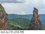 Towering rock formations stand prominently against a backdrop of rolling green hills and expansive sky. The sun casts a warm glow on the rugged stone, highlighting its textures and contrasts. Стоковое фото, фотограф Владимир Разгуляев / Фотобанк Лори