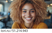 A cheerful woman with vibrant curly hair beams while sitting in an inviting office space filled with natural light. Стоковое AI-видео, аниматор Данила Большаков / Фотобанк Лори