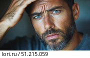 A man with striking blue eyes and a full beard contemplates as he touches his face in a dimly lit indoor setting. Стоковое AI-видео, аниматор Данила Большаков / Фотобанк Лори