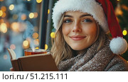 A young woman wearing a holiday hat enjoys a warm drink while reading a book next to a window adorned with twinkling lights. Стоковое AI-видео, аниматор Данила Большаков / Фотобанк Лори
