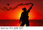 Silhouette of a soldier signaling to a helicopter with smoke flare while standing on shoreline. Oleg Zabielin / Stocktrek Images/TASS. Стоковое фото, агентство ТАСС / Фотобанк Лори