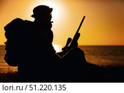 Silhouette of a special forces sniper sitting alert on the shoreline at sunset. Oleg Zabielin / Stocktrek Images/TASS. Стоковое фото, агентство ТАСС / Фотобанк Лори