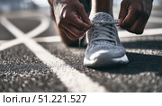 Male athlete carefully tying running shoe laces, concentrating before competitive track event, muscular hand gripping athletic footwear. Стоковое AI-изображение, AI-художник Юрий Поздников / Фотобанк Лори