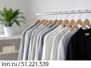 Neutral toned garments suspended from wooden hangers on metallic rack, embodying minimalist wardrobe philosophy with sustainable fashion sensibility. Стоковое AI-изображение, AI-художник Юрий Поздников / Фотобанк Лори