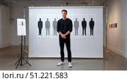 Young man is posing in an art gallery in front of an artwork representing human silhouettes with different shades of gray promoting diversity and inclusion. Стоковое AI-изображение, AI-художник Юрий Поздников / Фотобанк Лори