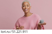 Female influencer showcasing small grey round object, wearing pink sweater, making expressive hand movements against pastel pink backdrop, blond hair styled short. Стоковое AI-видео, аниматор Юрий Поздников / Фотобанк Лори