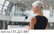 Professional senior businesswoman presenting conference keynote, speaking confidently in sleek black dress while sharing corporate insights with engaged listeners. Стоковое AI-видео, аниматор Юрий Поздников / Фотобанк Лори