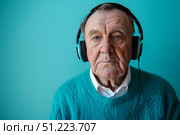 Пожилой мужчина с серьезным лицом в наушниках слушает музыку на бирюзовом фоне. Стоковое AI-изображение, AI-художник Кирилл Сиротюк / Фотобанк Лори