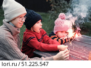 Children celebrating with colorful sparklers while dressed in warm clothing attire. Kids siblings enjoy the winter holidays outdoors. Festive evening. Christmas. New Year. Family Milestone Celebration. Стоковое фото, фотограф Марина Демидюк / Фотобанк Лори