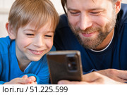 Father and son little boy laughing and using phone. They watching funny videos together, playing games on smartphone. Concept technology, smart phone addicted. Fun weekend activity. Modern fatherhood. Стоковое фото, фотограф Марина Демидюк / Фотобанк Лори