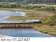 An old Soviet L-series steam locomotive. The Ruskeala Express retro train is driving along the lake. Side view from above. Russia, Republic of Karelia, Sortavala, August 11, 2025. Редакционное фото, фотограф Photojuli / Фотобанк Лори