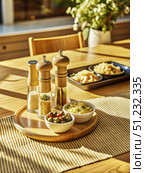 Three Salt and Pepper Shakers on a Wooden Tray With Small Dishes of Food on a Dining Table. Generative AI. Стоковое AI-изображение, AI-художник Roman Zavorotny / Фотобанк Лори