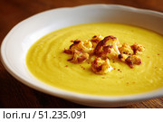 Cauliflower creamy soup with baked cauliflower florets on the top in a white bowl on a dark wood tabletop. Restaurant style dish. Hot, delicious plate of cream-of-cauliflower soup with melted cheese. Стоковое AI-изображение, AI-художник Марина Демидюк / Фотобанк Лори