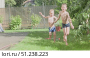 Children Joyfully Playing in Sprinkler Water During a Warm Summer Day Under the Sun. Стоковое видео, видеограф Olesia Kondrateva / Фотобанк Лори