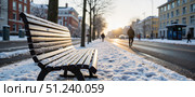 Snow-covered street in winter with people walking and a bench under sunlight. Стоковое AI-изображение, AI-художник Ольга Невская / Фотобанк Лори