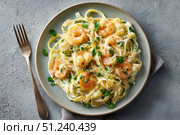 Shrimp Scampi. Spaghetti with shrimp and Creamy Garlic White Wine Sauce on a plate, top view. Scrumptious shrimp and fettuccine pasta with a cilantro, copy space. Linguine Alfredo. Italian cuisine. Стоковое AI-изображение, AI-художник Марина Демидюк / Фотобанк Лори