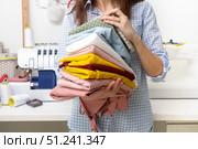 Sewing: a girl holds in her hands a stack of multi-colored fabrics on the background of a sewing machine. Стоковое фото, фотограф Енваев Андрей / Фотобанк Лори