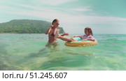 Mom and daughter laugh together as girl floats in donut ring. Pure beach joy, captured in turquoise water under sunny sky. Ideal image of summer vacation and loving family moment. Стоковое видео, видеограф Енваев Андрей / Фотобанк Лори