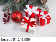 Three boxes with a gift tied with satin ribbons, a fir branch and Christmas tree decorations on a white background. Стоковое фото, фотограф Ирина Толокновская / Фотобанк Лори