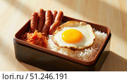 Bento box containing rice, sausages, kimchi and fried egg on wooden table. Стоковое фото, фотограф David Kashakhi / Фотобанк Лори