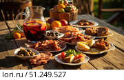 Sharing plates of iberian ham, olives, and bread with refreshing sangria on rustic wooden table. Стоковое фото, фотограф David Kashakhi / Фотобанк Лори