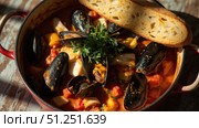 Delicious seafood stew simmering in red pot with crusty bread. Стоковое фото, фотограф David Kashakhi / Фотобанк Лори