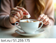 Руки молодой женщины кладут кубики сахара в белую чайную чашку. Атмосфера располагает к отдыху или чаепитию.. The hands of a young woman putting sugar cubes into a white teacup. The atmosphere is conducive to relaxing or having tea. Стоковое AI-изображение, AI-художник ketpro.design / Фотобанк Лори