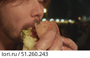 Extreme close-up captures hungry festival-goer eating juicy burger, focus on mouth and hands as he enjoys flavors during energetic night concert outdoors. Стоковое видео, видеограф Strunov David / Фотобанк Лори
