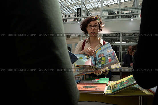 06.04.2023, Москва. Международная ярмарка интеллектуальной литературы «non/fictioNвесна» в Гостином дворе. Девушка показывает книгу посетителям выставки. Редакционное фото, фотограф Дмитрий Киселёв / Фотобанк Лори