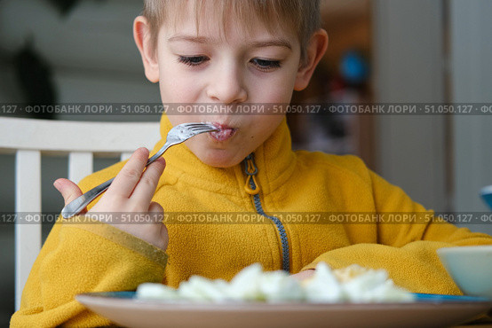 6 years old boy eats pasta with cheese from blue plate. Child is eating spaghetti. Lunch time. Good appetite. Tasty children food. Close-up portrait. Carbs dinner. Fast food. Kid eating with fork. Стоковое фото, фотограф Марина Демидюк / Фотобанк Лори