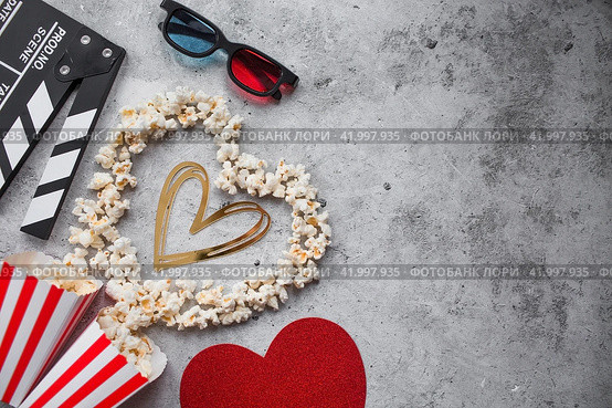 A banner for the film industry. A romantic movie date. A movie camera, 3D glasses, popcorn and a popcorn heart on a stylish concrete-gray background. The film will premiere on Valentine's Day. (2024 год). Стоковое фото, фотограф Photojuli / Фотобанк Лори