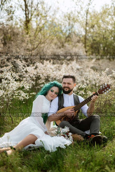 a bearded groom plays a stringed instrument and a girl with green hair sits in a spring meadow. Стоковое фото, агентство Ingram Publishing / Фотобанк Лори