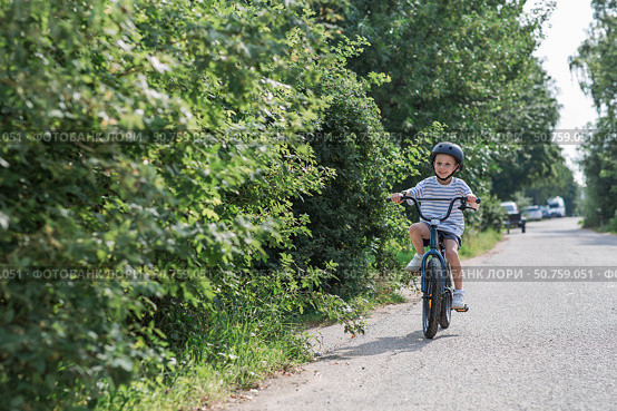 A beautiful 6-year-old boy riding a bicycle in a protective helmet outside. A happy child engaged in an active sport. Protection. Life insurance and child safety. Стоковое фото, фотограф Photojuli / Фотобанк Лори