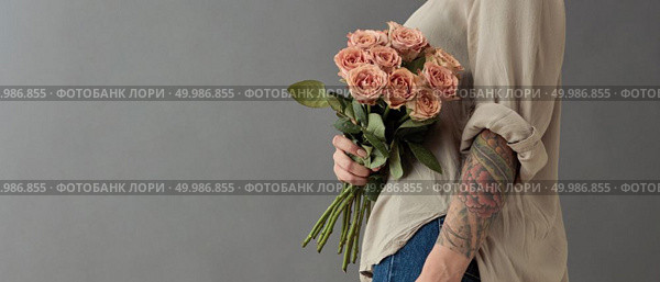 A beautiful bouquet of beige roses cappuccino.The woman is holding flowers in her hand tatoo on a gray background. Mother’s Day, Valentine’s Day. A beautiful bouquet of beige roses cappuccino. Стоковое фото, агентство Ingram Publishing / Фотобанк Лори