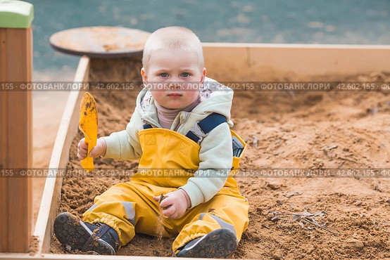 A beautiful, cheerful little boy of two years old walks on the playground in the spring. A child is playing with a shovel in the sandbox. The concept of parenthood, happy childhood and family. Стоковое фото, фотограф Photojuli / Фотобанк Лори