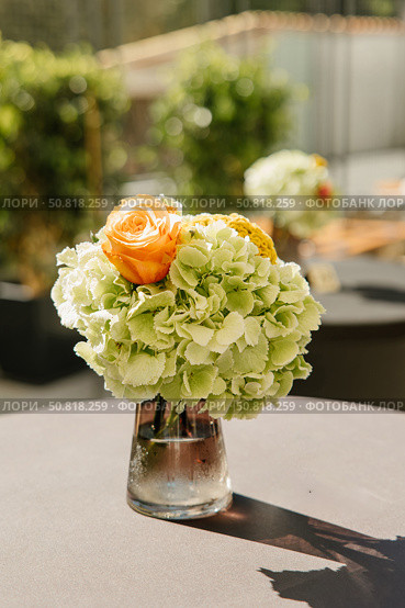 A beautifully arranged floral centerpiece featuring vibrant orange roses and delicate green hydrangeas in a glass vase, perfect for enhancing any elegant setting. Стоковое фото, фотограф Башкирова Анна / Фотобанк Лори