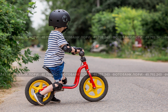 A cheerful little boy rides a running bike in a helmet outdoors. A happy child is engaged in an active sport. Protection. Life insurance and child safety. Стоковое фото, фотограф Photojuli / Фотобанк Лори